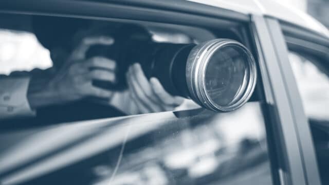Detektiv in einem Auto macht mit einer Kamera ein Bild