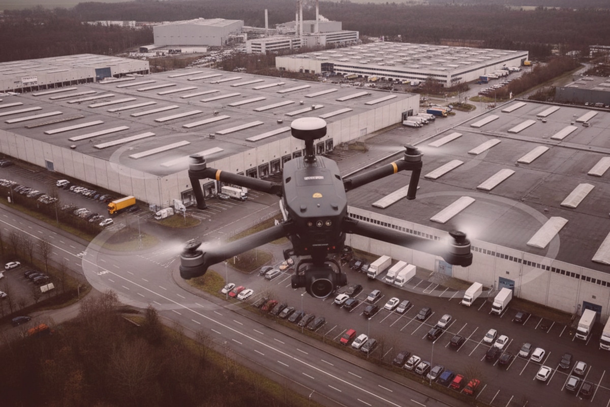 Detektei nutzt schwarze Drohne mit Kamera zur Überwachung eines Industriekomplexes, Lagerhallen und Fahrzeuge aus der Luft bei Tag.