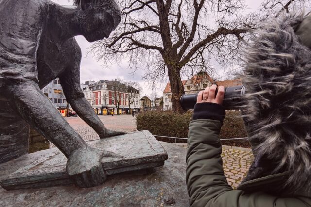 Detektivin der Detektei Bergisch Gladbach fotografiert eine Zielperson auf dem Konrad-Adenauer-Platz Bergisch Gladbach neben der Sehenswürdigkeit Papierschöpfer während einer Observation.