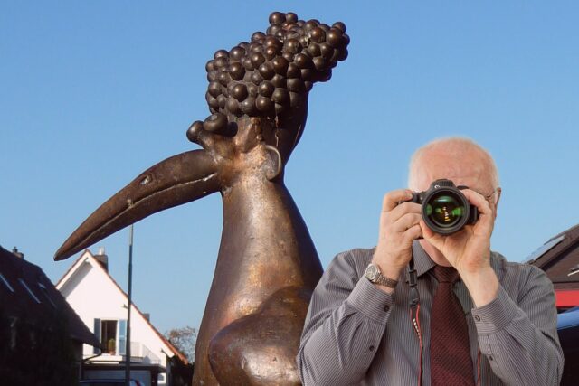 Detektei Kubon ermittelt in Friedelsheim, Detektiv der Detektei fotografiert, Bürgerbrunnen Friedelsheim im Hintergrund, Schriftzug: Wir ermitteln für Sie in Friedelsheim!