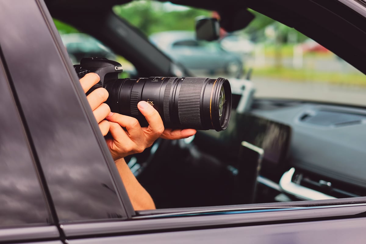 Detektiv mit Kamera und Teleobjektiv fotografiert unauffällig aus dem Auto - diskrete Beobachtung durch Ermittler einer Detektei.