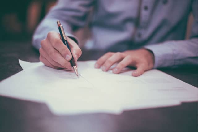 Person mit Stift an einem Tisch. Unterschreibt Aufhebungsvertrag