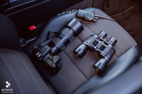 privatdetektiv-ausruestung Kamera Fernglas Funkgerät liegen auf Autositz